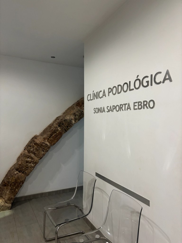Sala de espera de la clínica con sillas transparentes y parte del arco de piedra de la pared visible.